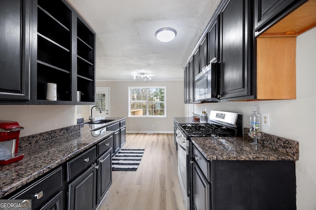 kitchen featuring appliances with stainless steel finishes, sink, light wood-type flooring, and dark stone counters