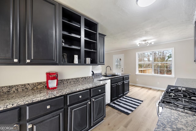 kitchen with sink, dark stone countertops, ornamental molding, stainless steel appliances, and light wood-type flooring