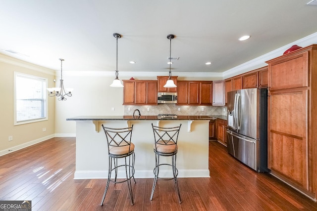 kitchen featuring pendant lighting, stainless steel appliances, an island with sink, and a breakfast bar