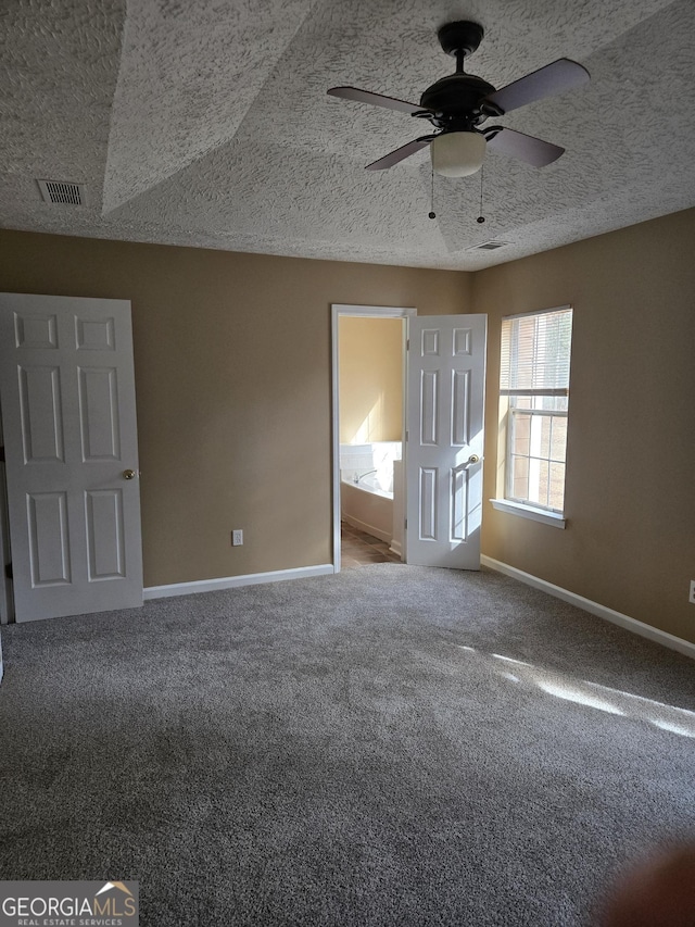 unfurnished bedroom featuring ceiling fan, ensuite bathroom, a textured ceiling, and carpet