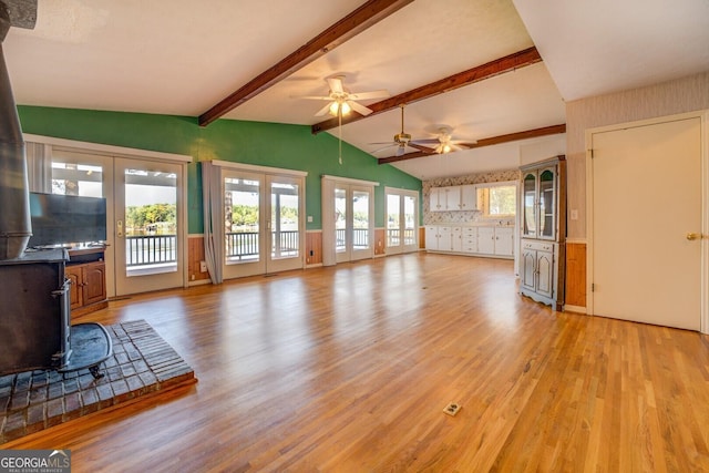 unfurnished living room with french doors, vaulted ceiling with beams, light hardwood / wood-style flooring, a wood stove, and ceiling fan