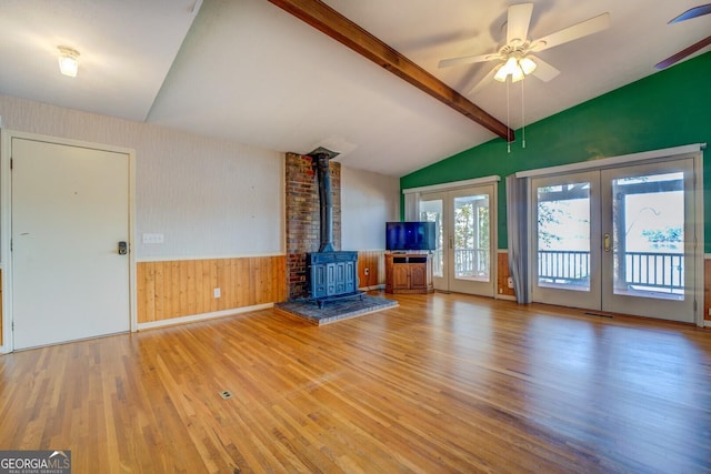 unfurnished living room featuring french doors, vaulted ceiling with beams, light wood-type flooring, a wood stove, and ceiling fan