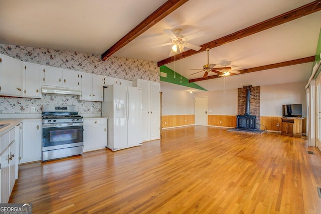 kitchen with stainless steel gas stove, white fridge with ice dispenser, white cabinets, and a wood stove