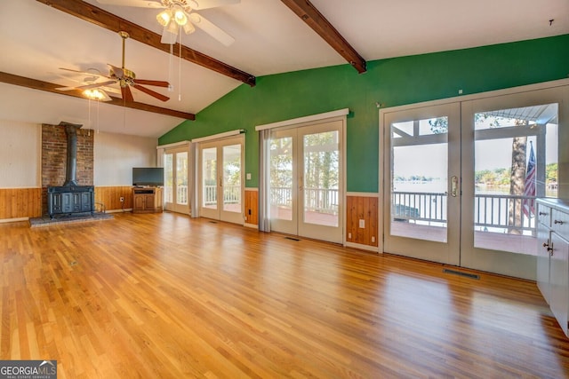 unfurnished living room featuring lofted ceiling with beams, a wood stove, light hardwood / wood-style flooring, and french doors