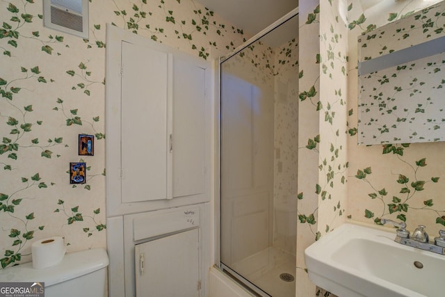 bathroom with a shower with door, sink, and toilet