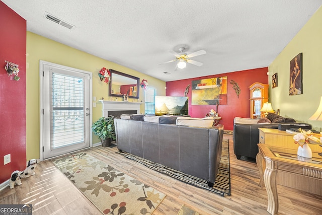 living room with ceiling fan, a textured ceiling, and light wood-type flooring