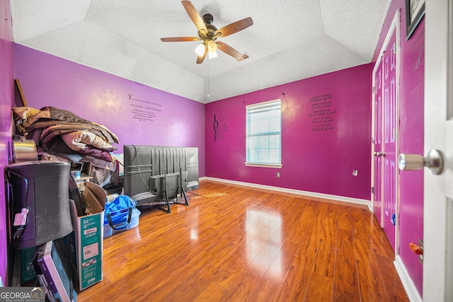 bedroom with lofted ceiling, a textured ceiling, a raised ceiling, ceiling fan, and hardwood / wood-style floors