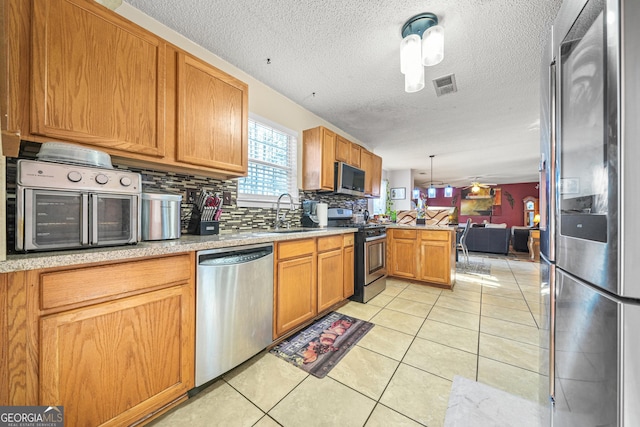 kitchen with light tile patterned flooring, sink, decorative light fixtures, kitchen peninsula, and stainless steel appliances