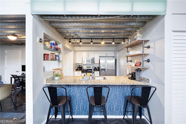 kitchen with stainless steel appliances, sink, white cabinets, and a kitchen bar