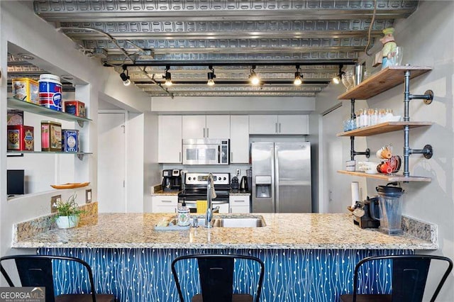 kitchen featuring stainless steel appliances, white cabinetry, light stone counters, and kitchen peninsula