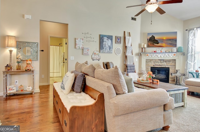 living room featuring ceiling fan, a stone fireplace, high vaulted ceiling, and light hardwood / wood-style floors