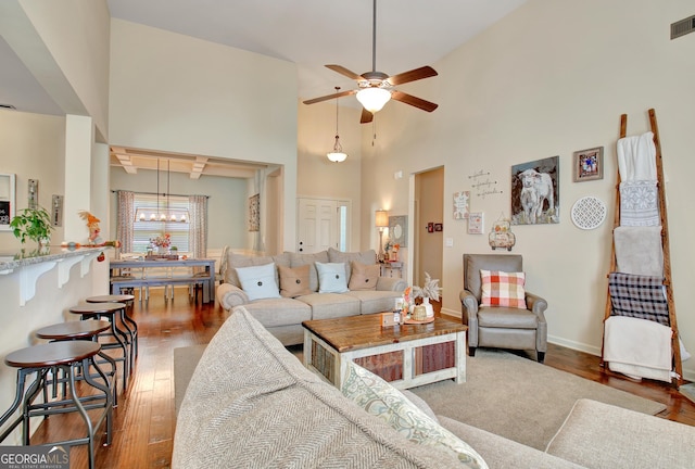 living room featuring dark hardwood / wood-style floors, ceiling fan with notable chandelier, and a high ceiling