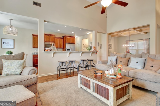 living room featuring coffered ceiling, a towering ceiling, beamed ceiling, ceiling fan, and light hardwood / wood-style floors