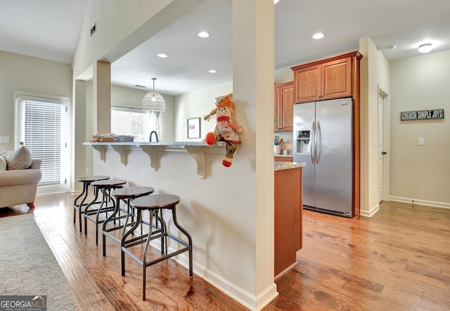 kitchen featuring pendant lighting, a breakfast bar area, light hardwood / wood-style floors, stainless steel fridge with ice dispenser, and kitchen peninsula