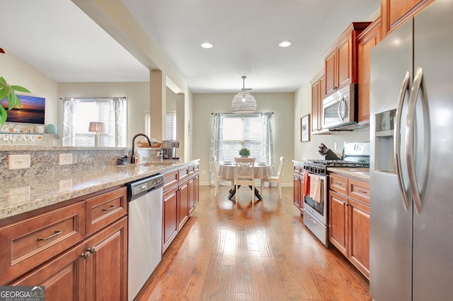 kitchen featuring sink, hanging light fixtures, light hardwood / wood-style flooring, stainless steel appliances, and light stone countertops