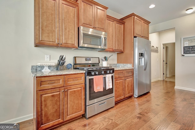 kitchen featuring appliances with stainless steel finishes, light stone countertops, and light hardwood / wood-style flooring