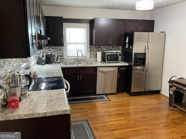 kitchen featuring sink, light hardwood / wood-style flooring, appliances with stainless steel finishes, decorative backsplash, and exhaust hood