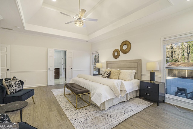bedroom featuring crown molding, wood finished floors, multiple windows, and a raised ceiling