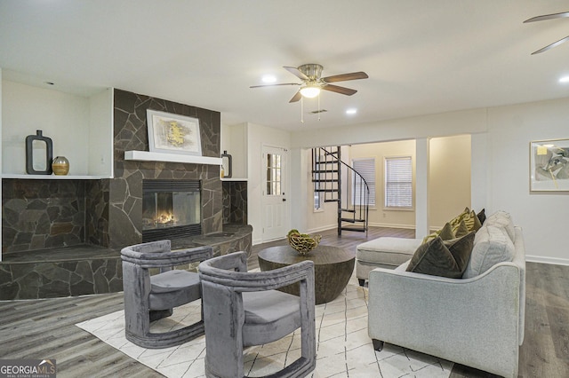 living area featuring baseboards, a ceiling fan, wood finished floors, stairway, and a stone fireplace