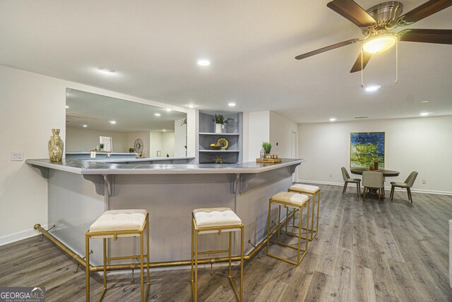 kitchen with recessed lighting, a kitchen bar, wood finished floors, and baseboards