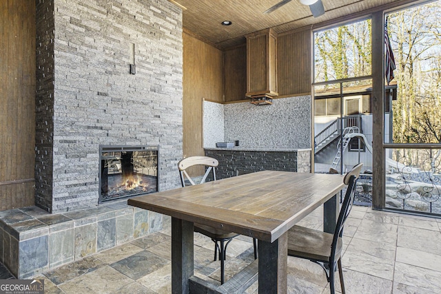 dining space with a ceiling fan, stone tile floors, wood ceiling, a fireplace, and a high ceiling