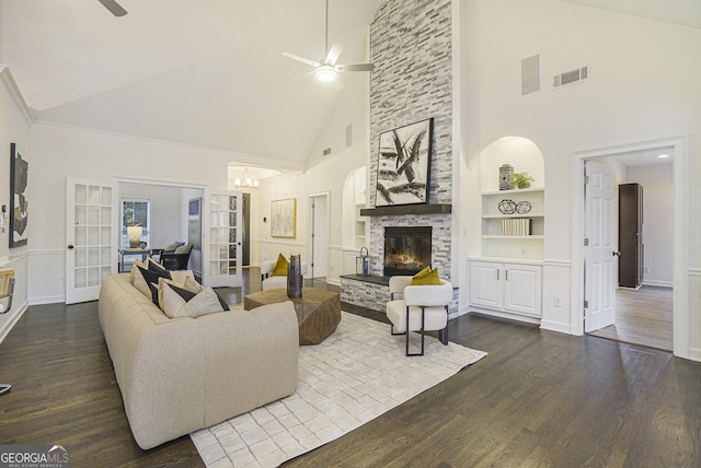 living room with dark wood finished floors, high vaulted ceiling, a stone fireplace, built in shelves, and ceiling fan with notable chandelier