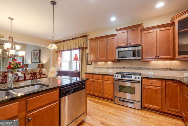 kitchen featuring hanging light fixtures, appliances with stainless steel finishes, glass insert cabinets, a sink, and dark stone counters