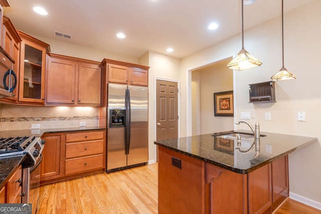 kitchen featuring decorative light fixtures, stainless steel appliances, a sink, brown cabinets, and glass insert cabinets