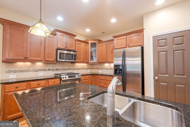 kitchen with stainless steel appliances, a sink, dark stone counters, glass insert cabinets, and pendant lighting