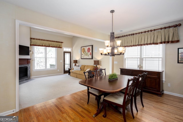 dining space with light wood-style flooring, light carpet, a fireplace with flush hearth, baseboards, and an inviting chandelier