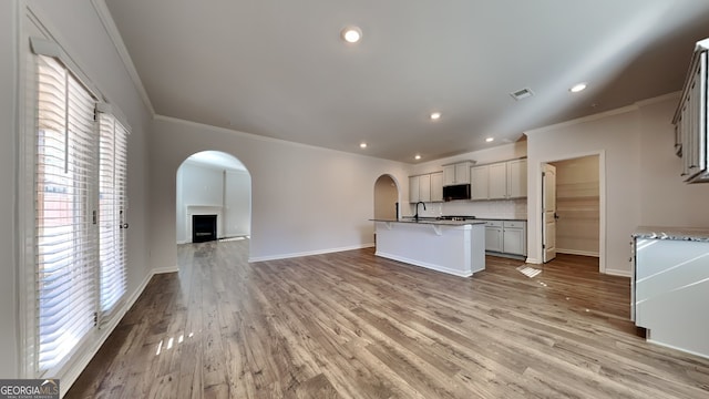 kitchen featuring sink, a kitchen island with sink, tasteful backsplash, ornamental molding, and light hardwood / wood-style floors