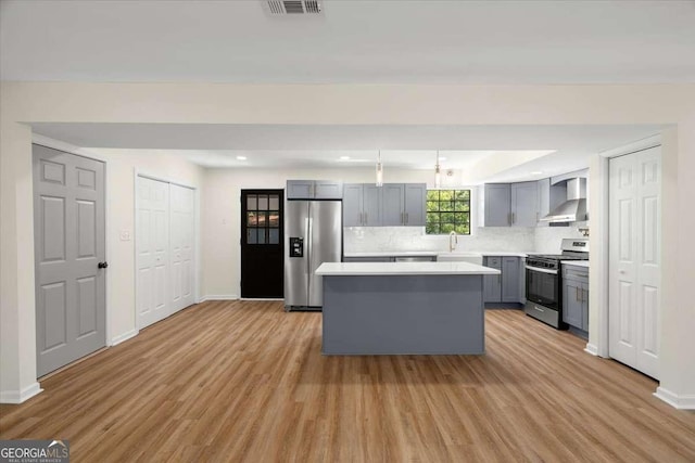 kitchen featuring gray cabinets, appliances with stainless steel finishes, a center island, wall chimney exhaust hood, and light hardwood / wood-style flooring