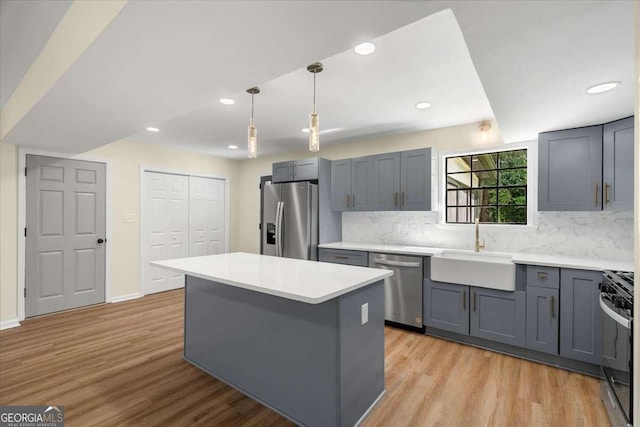 kitchen with a kitchen island, appliances with stainless steel finishes, sink, hanging light fixtures, and light hardwood / wood-style floors