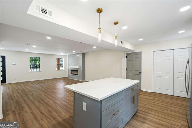 kitchen with a kitchen island, dark hardwood / wood-style floors, pendant lighting, a large fireplace, and gray cabinetry