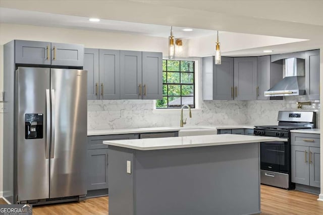 kitchen featuring wall chimney exhaust hood, sink, decorative light fixtures, a center island, and appliances with stainless steel finishes