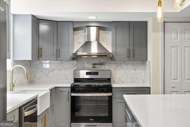 kitchen with pendant lighting, gray cabinets, appliances with stainless steel finishes, tasteful backsplash, and wall chimney exhaust hood