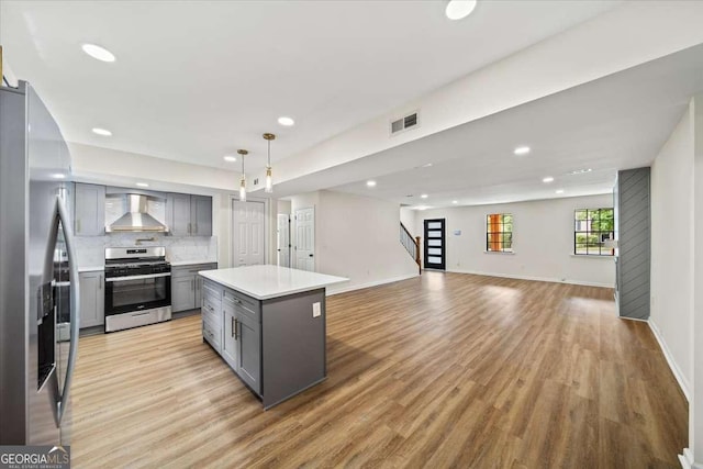 kitchen featuring a kitchen island, pendant lighting, gray cabinetry, stainless steel appliances, and wall chimney range hood