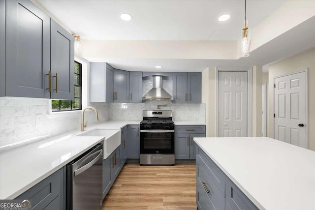 kitchen featuring sink, gray cabinets, hanging light fixtures, stainless steel appliances, and wall chimney exhaust hood