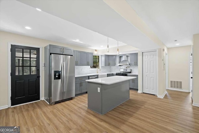 kitchen featuring gray cabinetry, decorative light fixtures, a center island, stainless steel appliances, and wall chimney range hood