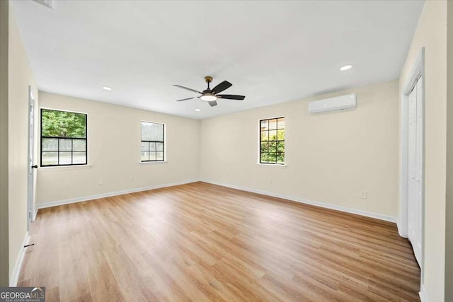 spare room featuring ceiling fan, a wall mounted AC, and light hardwood / wood-style floors