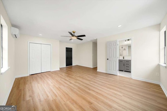 unfurnished bedroom with connected bathroom, a wall mounted air conditioner, light wood-type flooring, multiple closets, and ceiling fan