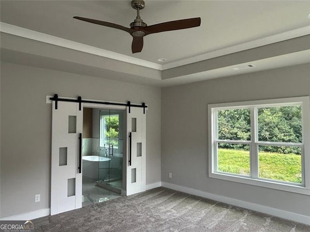 unfurnished bedroom with carpet flooring, a barn door, a raised ceiling, and multiple windows