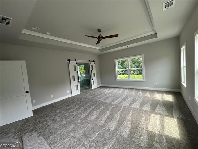 carpeted empty room with a raised ceiling, ceiling fan, and a barn door