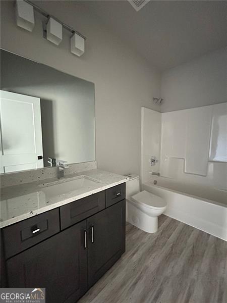 full bathroom featuring hardwood / wood-style flooring, bathing tub / shower combination, vanity, and toilet