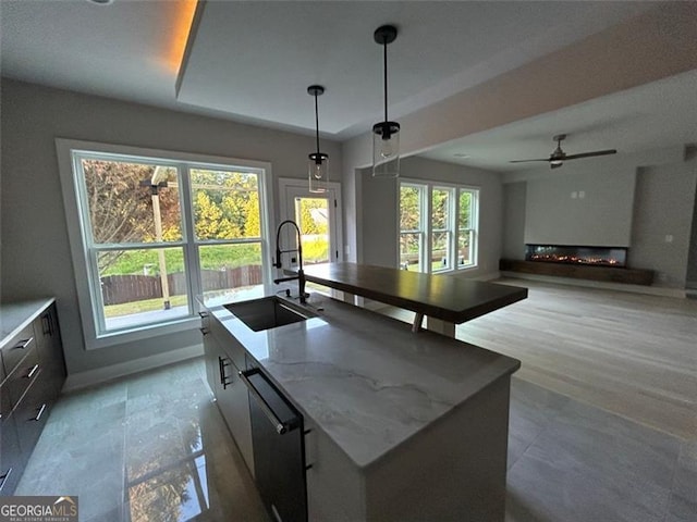 kitchen with decorative light fixtures, dishwasher, sink, a kitchen island with sink, and light stone counters