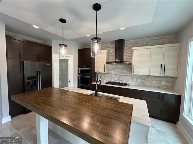 kitchen with dark brown cabinetry, sink, pendant lighting, wall chimney range hood, and backsplash