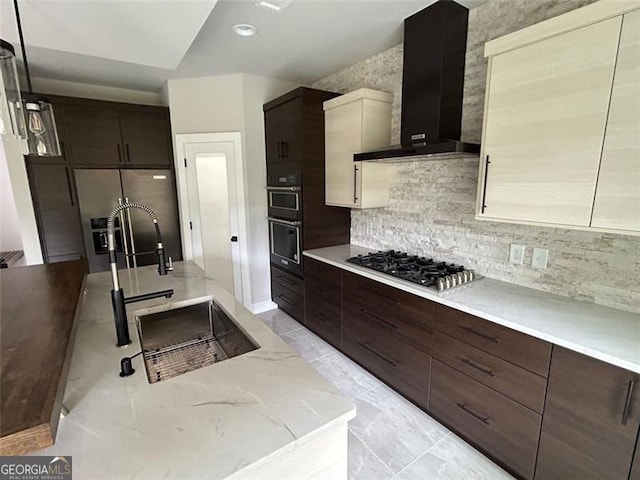 kitchen featuring wall chimney range hood, sink, stainless steel appliances, tasteful backsplash, and light stone counters