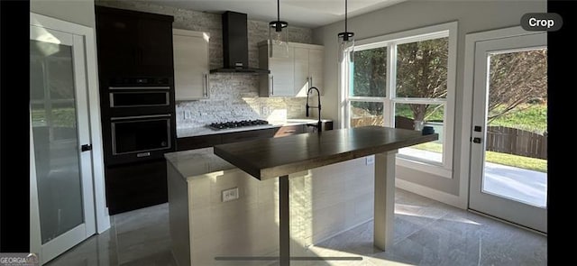 kitchen featuring pendant lighting, stainless steel gas stovetop, sink, white cabinets, and wall chimney exhaust hood