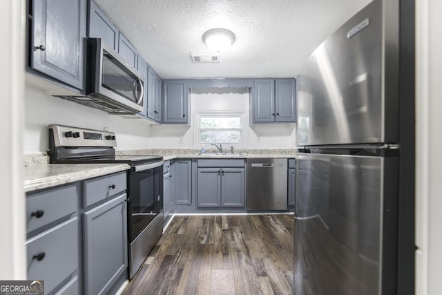 kitchen with sink, a textured ceiling, appliances with stainless steel finishes, dark hardwood / wood-style floors, and gray cabinets