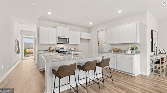 kitchen featuring appliances with stainless steel finishes, white cabinetry, a kitchen island with sink, and sink